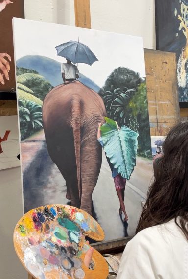 Elefante y persona caminando por un paisaje, ambos con paraguas. Paleta de pintor en primer plano.