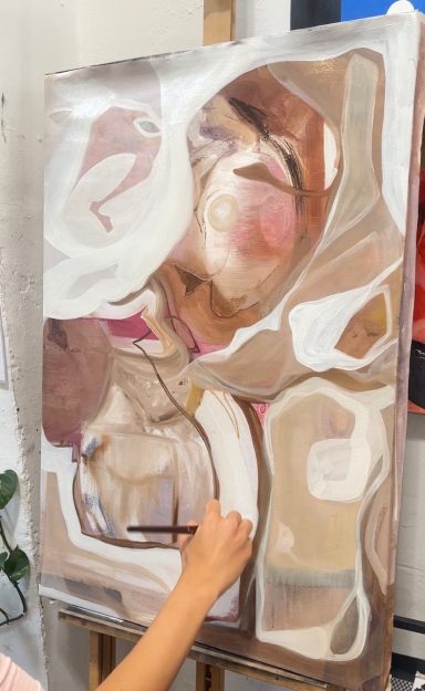 Una persona está pintando un cuadro abstracto con tonos marrones y formas fluidas.